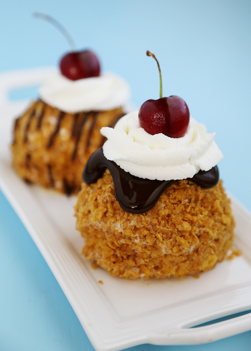 Easy Mexican Fried Ice Cream - Creamy ice cream rolled in crispy cornflakes, topped with chocolate, cream and cherries. So easy + elegant! Thecomfortofcooking.com