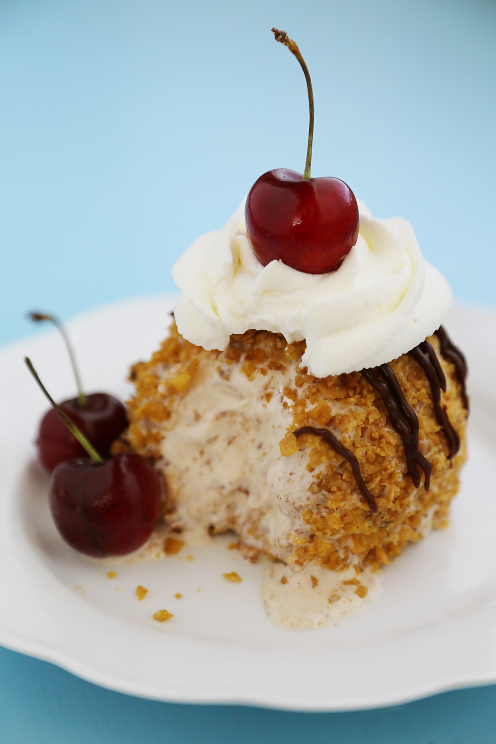 Easy Mexican Fried Ice Cream - Creamy ice cream rolled in crispy cornflakes, topped with chocolate, cream and cherries. So easy + elegant! Thecomfortofcooking.com